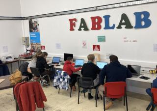Des enfants sont devant des ordinateurs. Sur le mur au dessus d'eux, on peut lire "Fablab"