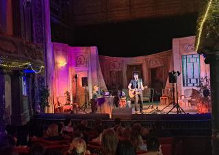 Vue depuis la salle de deux personnes sur une scène de théâtre, avec les décors et la lumière d'un spectacle