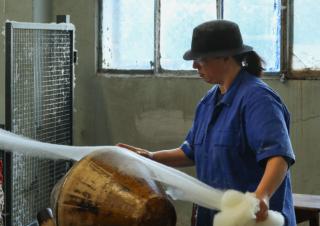 Une personne coiffée d'un chapeau tient un voile de textile qu'elle appose sur un tour de bois