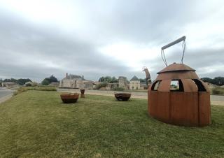 Une théière géante en métal sur une pelouse, au loin, un château