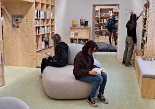 Des personnes sont assises et lisent sur un pouf, entourés d'étagères remplies de livres
