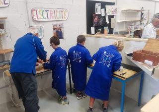 Quatre personnes en blouse bleue dans un atelier, parmi eux trois enfants