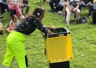 Une personne pousse une poubelle à couvercle jaune devant d'autres personnes assises