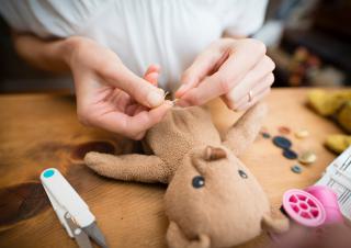 Des mains qui recoudent un ours en peluche