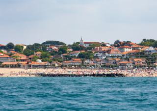 Vue depuis la mer d'une plage avec en fond un village et des colines