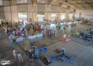 Dans une vaste halle, des stands sont installés et des gens se promènent