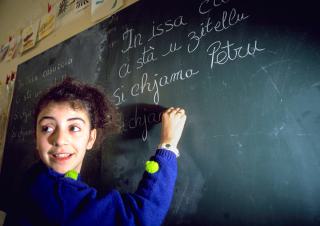 une petite fille écrit en langue Corse au tableau 