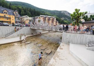 Vue d'un cours d'eau surmonté d'une passerelle, avec des personnes auprès de la passerelle et un enfant qui marche dans le cours d'eau
