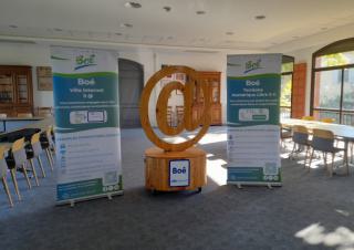 Un grand signe arobase en sculpture, entouré de deux panneaux, dans une salle type salle de réunion