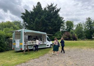 Un camion type food-truck sur une pelouse, deux personnes marchent vers le côté ouvert du camion