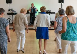 Au premier plan, des personnes dansent face à un monsieur qui joue de l'accordéon