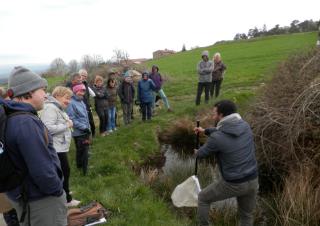 Des personnes regardent un homme qui manie une pelle, dans un pré