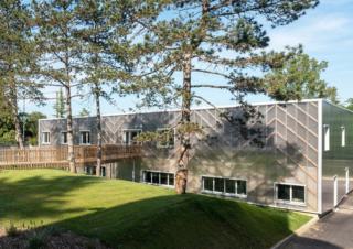 Un bâtiment parallélépipédique moderne, bordée d'une pelouse et de pins maritimes