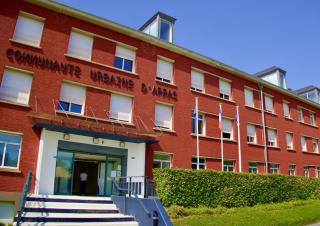 Façade d'un batiment long, haut de trois étage, rouge, sur lequel on peut lire "Communauté urbaine d'Arras"
