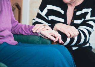 plan rapporché, pas de visages visibles, deux personnes se tiennent les mains. Une des personnes a beaucoup de rides sur les mains