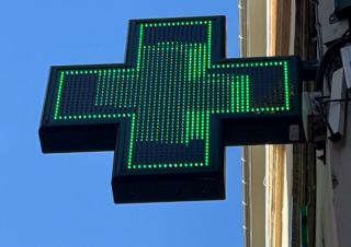 Une enseigne lumineuse enforme de croix verte, sur fond de ciel bleu