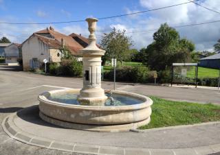 Une fontaine avec un bassin rond, sur un terre-plein entre des rues