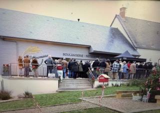Des personnes se tiennent devant un bâtiment sur lequel on peut lire "boulangerie"