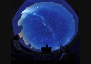 Un rond de ciel étoilé se démarque de l'ombre, avec des silhouettes de personnes