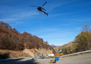 Un hélicoptère tracte un pylone, dans une zone entourée de montagnes
