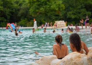 Deux jeunes femmes en maillot de bain, de dos face à un plan d'eau, avec des baigneurs